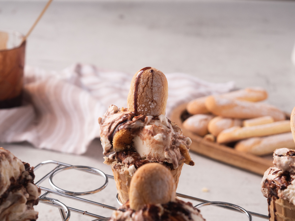 zbliżenie na lody tiramisu w wafelku, polane syropem kawowym, udekorowane biszkopcikiem