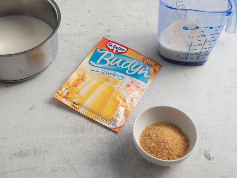 Na blacie kuchennym budyń, obok cukier trzcinowy i mleko.