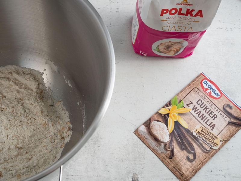 W metalowej misie składniki na kruszonkę. Obok cukier z wanilią i mąka na blacie.