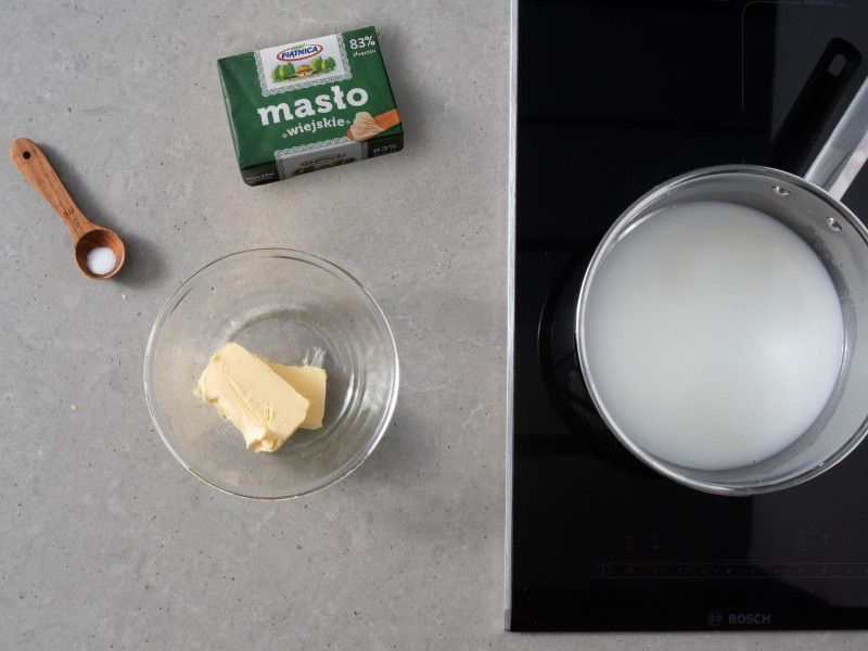W garnku mleko z wodą. Obok kostka masła. Szczypta soli i cukru na łyżeczce i pokrojone masło z misce.