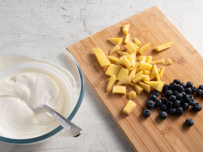 Rozmieszany jogurt z wanilią, a obok na desce mango i borówki.