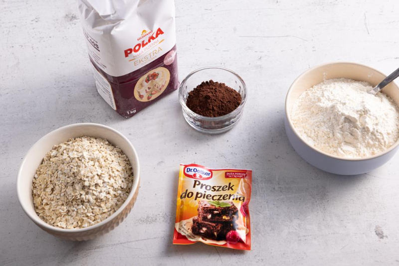 Na blacie kuchennym mąka pszenna, płatki owsiane, proszek do pieczenia i kakao.