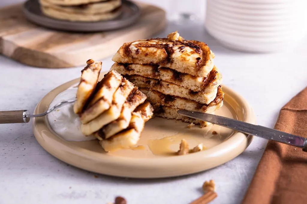 Przekrojone na pół pancakes cynamonka ze skyrem, syropem klonowym i posypane orzeszkami - przepis Wszystkiego Słodkiego