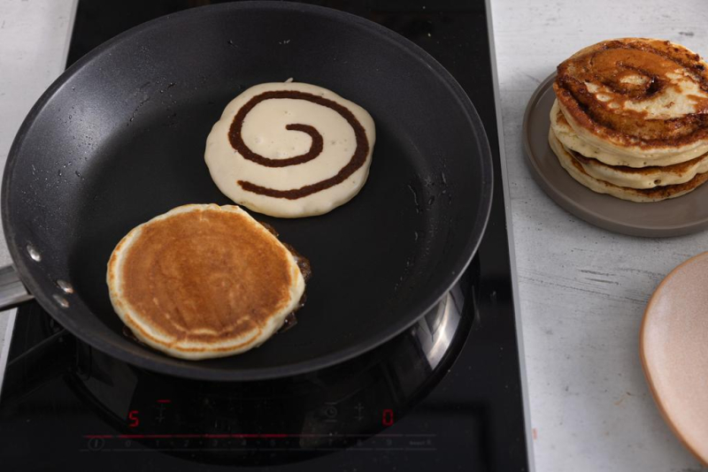 Smażenie pancakes na patelni. Obok na talerzyku już gotowe, usmażone pancakes.