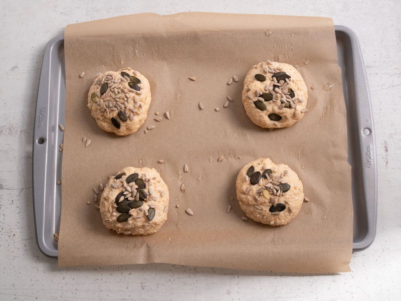 na blaszce uformowane bułeczki z serka wiejskiego posypane ziarnami