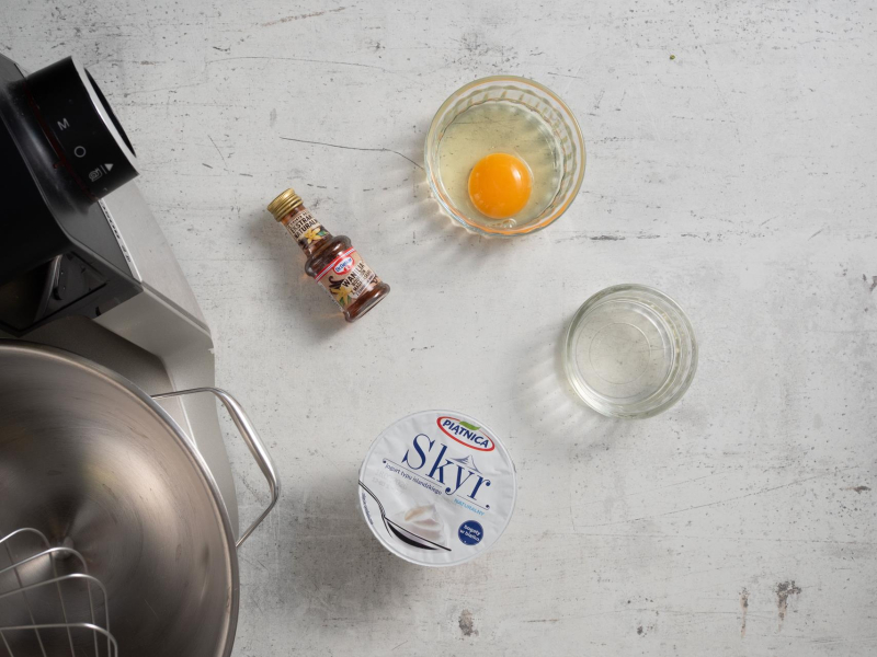 Na blacie kuchennym opakowanie skyru, jajko, ekstrakt waniliowy i spirytus w pojemniczku.
