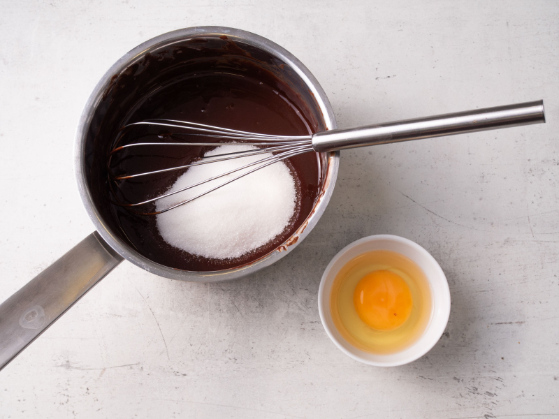 w rondelku masa czekoladowa i cukier, obok jajko