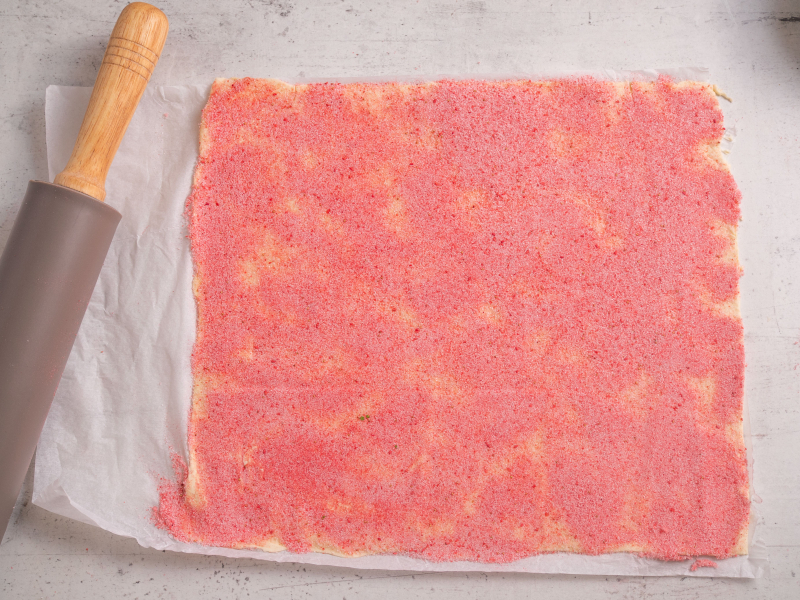 wałek do ciasta, obok arkusz ciasta francuskiego posypany różowym cukrem