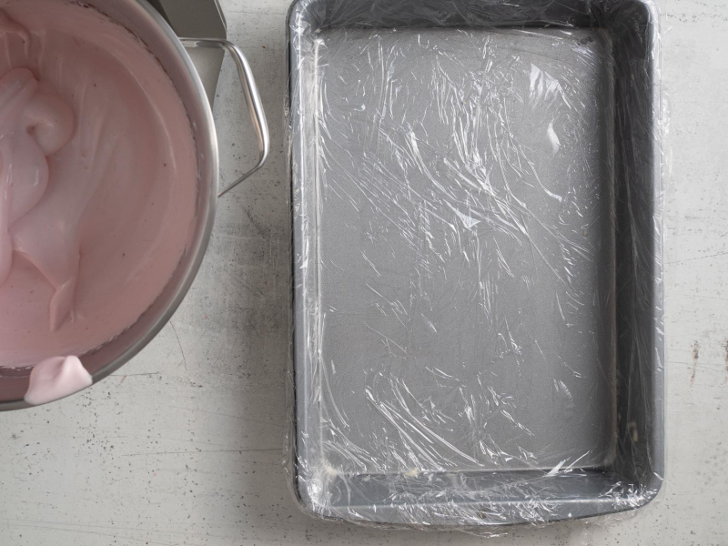Prostokątna forma wyłożona folią spożywczą. Obok ubita masa.
