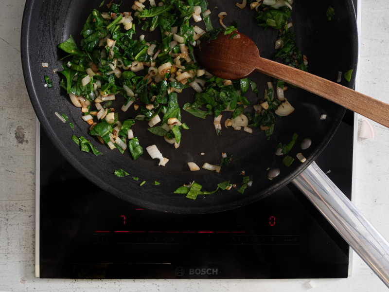 Smażenie szpinaku z cebulą i czosnkiem na patelni.