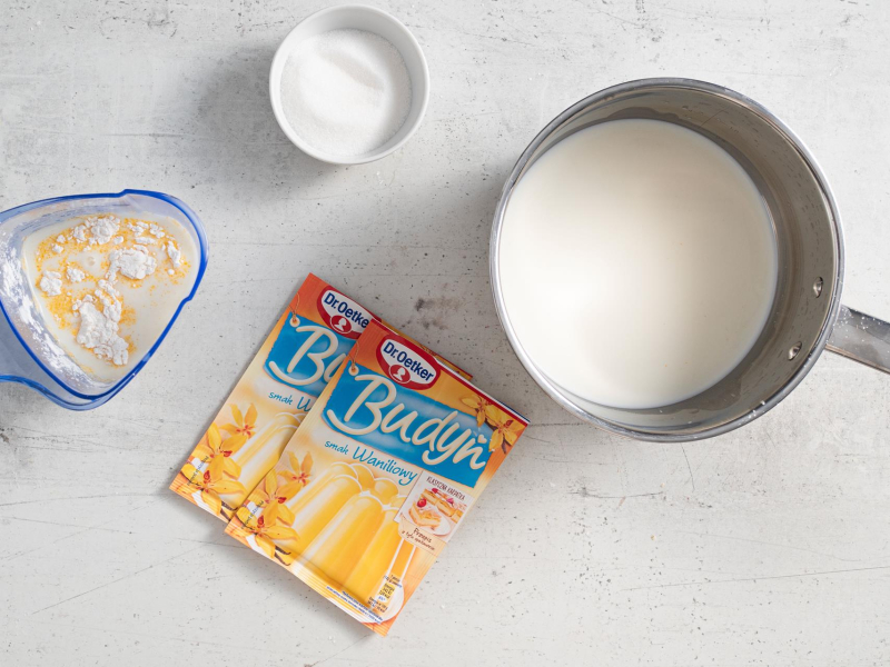 Na blacie kuchennym budynie, mleko w garnku, cukier w miseczce .